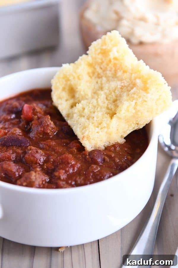 The Ultimate Cornbread with Cloudlike Honey Butter 3 A generous piece of cornbread resting beside a steaming bowl of chili, illustrating a perfect pairing.