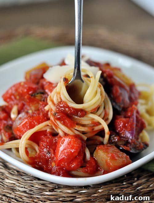 Balsamic Roasted Vegetable Pasta Sauce 2 A plate of perfectly cooked spaghetti generously coated with a chunky, rich red pasta sauce, with a fork poised to take a delicious bite from the center.