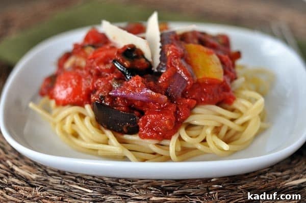 Balsamic Roasted Vegetable Pasta Sauce 3 A crisp white plate laden with cooked spaghetti noodles, generously topped with a rich, chunky red sauce and ready to be enjoyed.