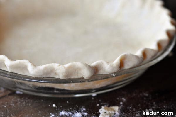 The Ultimate Pie Crust Recipe and Guide 3 Side view of a beautifully crimped uncooked pie crust in a glass pie dish.