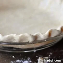 The Ultimate Pie Crust Recipe and Guide 9 Side view of an uncooked crimped pie crust in a glass pie dish.