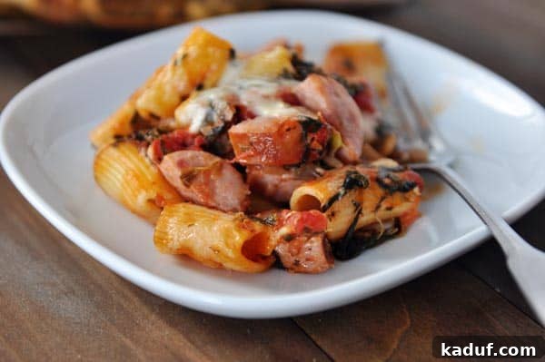 Hearty Chicken Sausage Pasta Bake 3 White plate with cooked tube pasta, slices of chicken sausage, and melted cheese, garnished with fresh herbs.