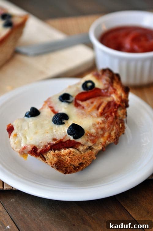 Elevated French Bread Pizza 3 A slice of cooked pepperoni olive french bread pizza on a white plate.