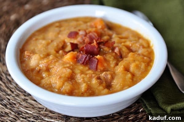 A close-up of a white bowl featuring a rich serving of ham, sweet potato, bacon, and white bean soup, highlighting its texture and ingredients.