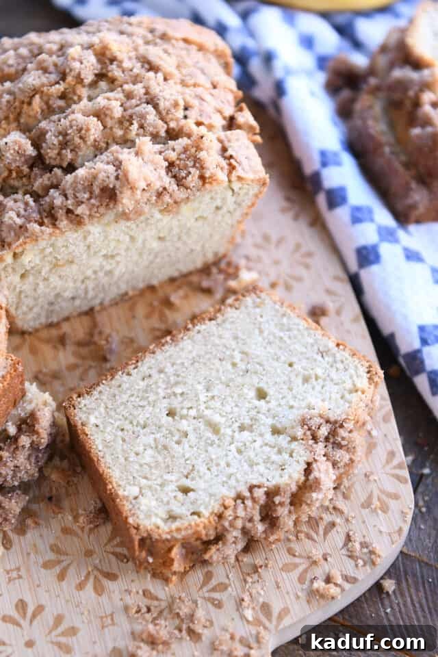 Cream Cheese Swirl Banana Bread with Cinnamon Crumble 2 A perfectly sliced piece of cream cheese banana bread, revealing its moist crumb and topped with a glistening cinnamon streusel, resting on a rustic wooden cutting board, ready to be enjoyed.