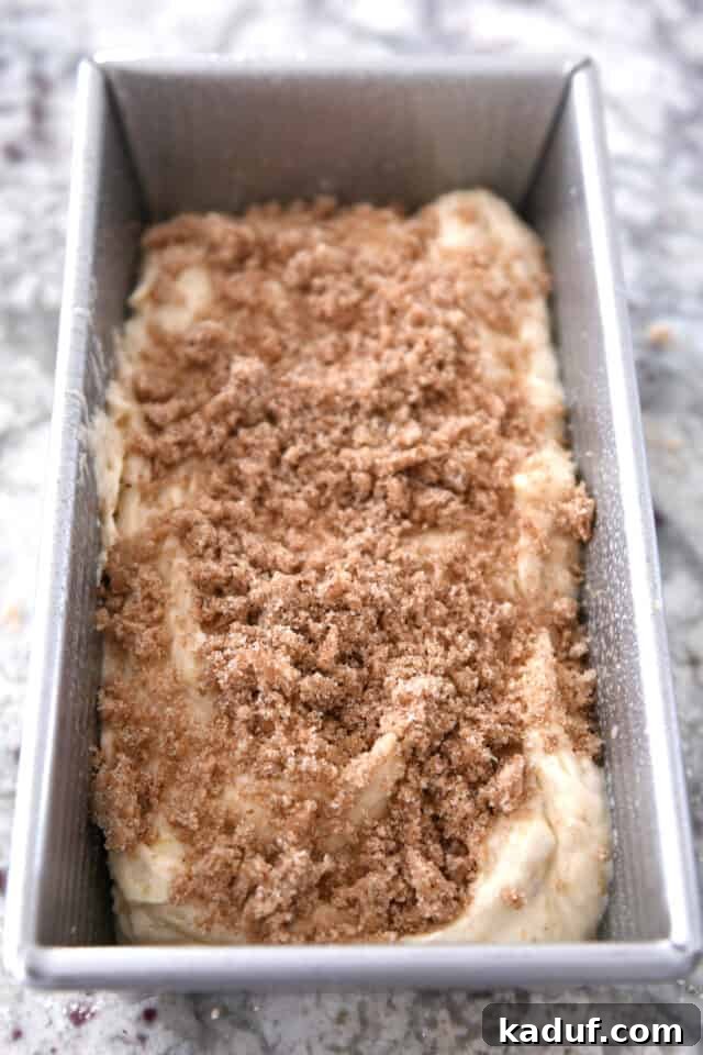 Cream Cheese Swirl Banana Bread with Cinnamon Crumble 7 Raw banana bread batter, perfectly portioned and settled in a bread pan, generously topped with the sweet cinnamon streusel mixture, eagerly awaiting its transformation in the oven.