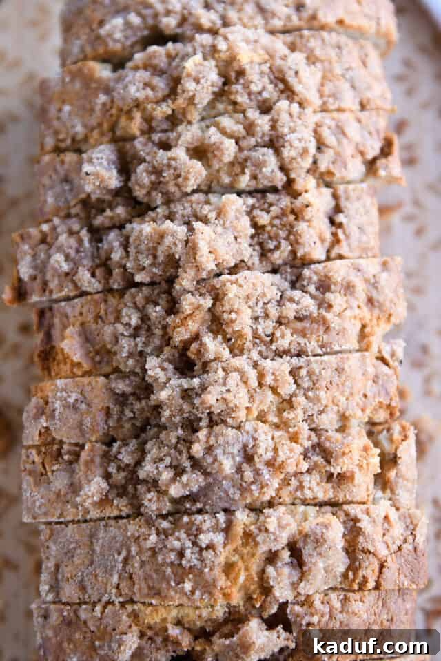 Cream Cheese Swirl Banana Bread with Cinnamon Crumble 9 An inviting top-down view of seven perfectly cut slices of cream cheese banana bread, each adorned with a sweet cinnamon streusel, arranged neatly on a rustic wooden surface, highlighting its appetizing appearance.