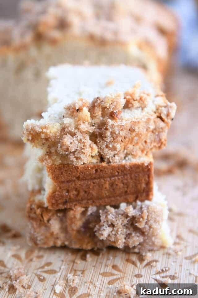 Cream Cheese Swirl Banana Bread with Cinnamon Crumble 10 Three beautifully stacked half slices of cream cheese banana bread, showcasing the golden crumb and tempting cinnamon topping, artfully arranged on a textured wooden cutting board.