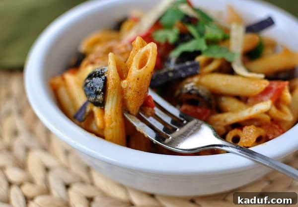 Southwestern Chicken Pasta 3 A fork holding a bite of cheesy, saucy penne pasta with chicken, ready to be eaten from a white bowl.
