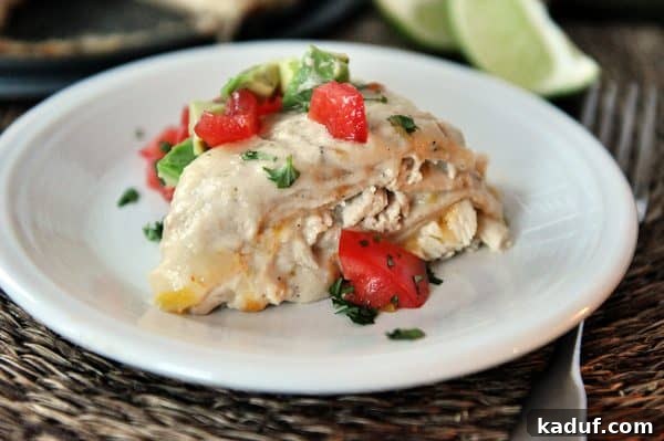 Green Chile Chicken Enchilada Tower 3 A generous slice of green chile chicken enchilada stack rests on a white plate, adorned with vibrant red tomatoes and green cilantro, highlighting its inviting layers.