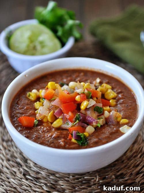 White bowl full of fire-roasted tomato and black bean soup topped with fresh corn salsa.