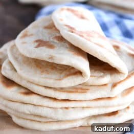 Delicious Homemade Flatbread 11 A stack of golden brown flatbread on a wooden cutting board. The top two flatbreads are folded in half. A blue and white checkered towel is laying beside the bread.