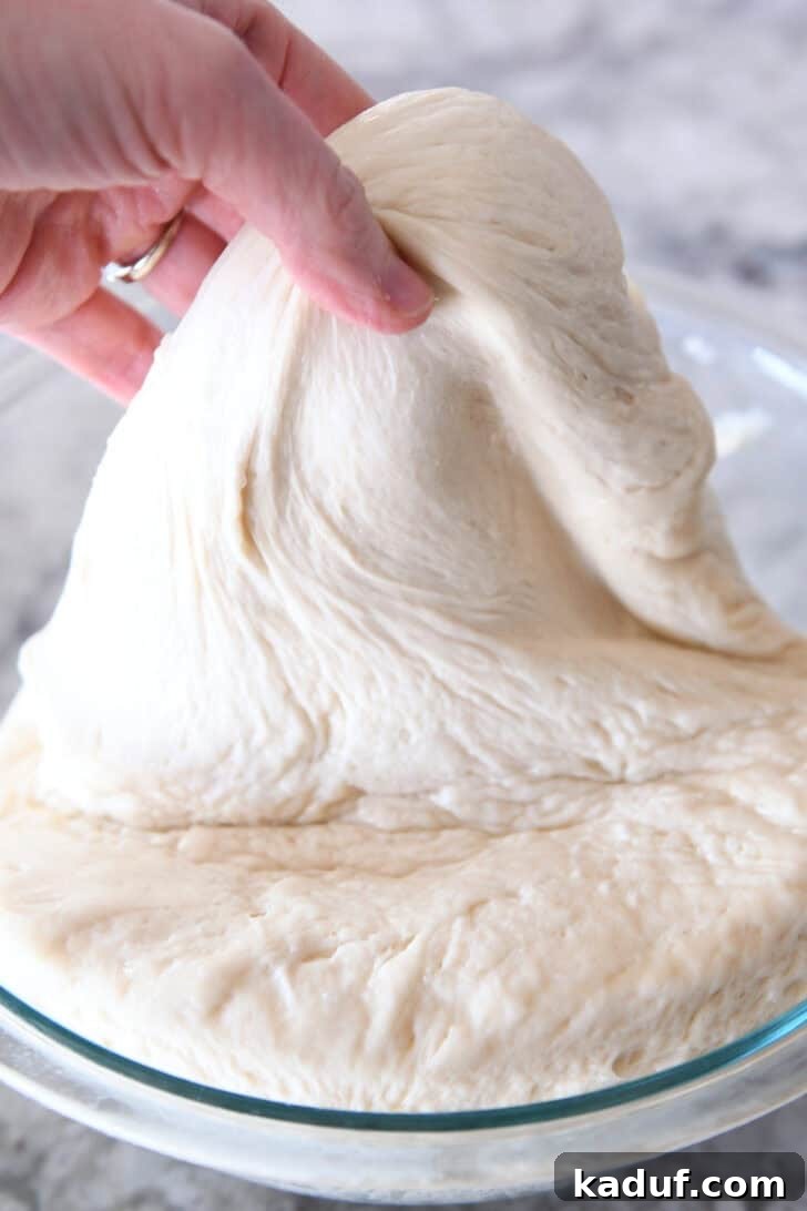Delicious Homemade Flatbread 4 A hand pulling bread dough out of a glass bowl.