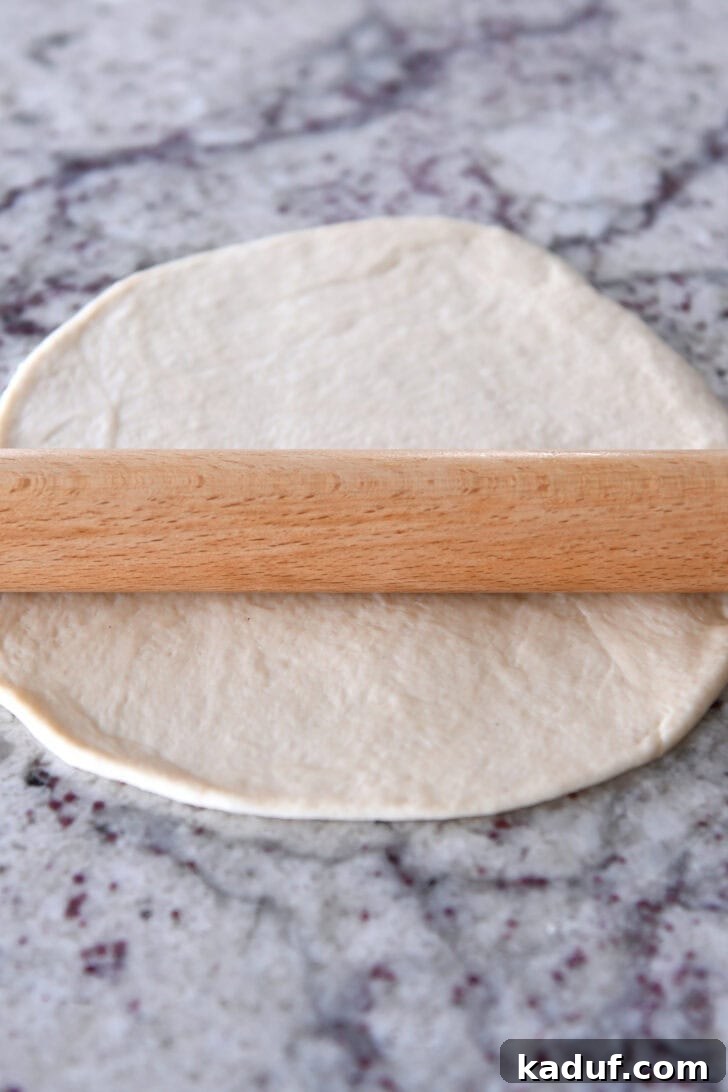 Delicious Homemade Flatbread 6 A wooden rolling pic rolling out bread dough into a circle on a granite countertop.