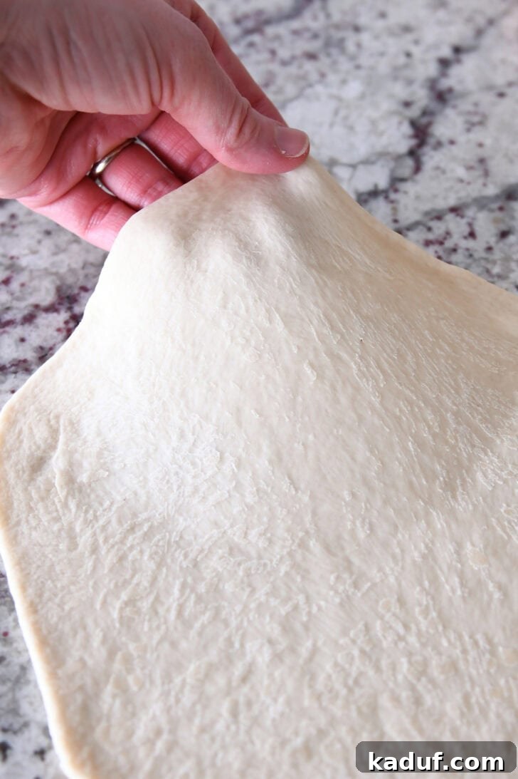 Delicious Homemade Flatbread 7 A hand pulling the side of a rolled out piece of bread dough up off the counter.