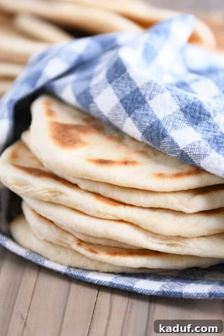 Delicious Homemade Flatbread 9 A stack of golden brown flatbreads wrapped in a blue and white checkered kitchen towel.