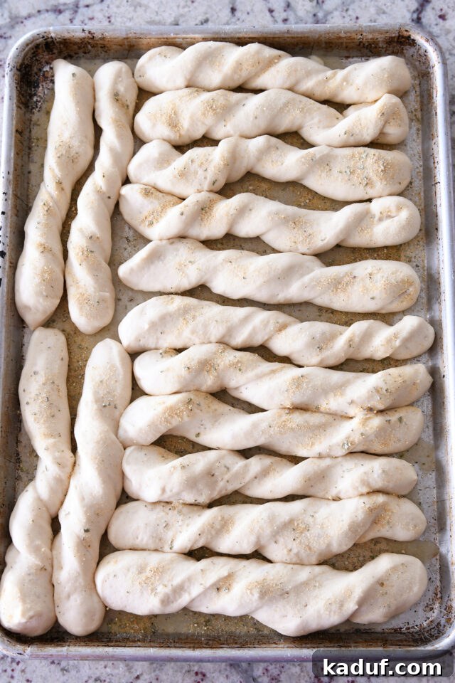 Heavenly 60-Minute Homemade Breadsticks 5 A baking sheet filled with perfectly shaped breadsticks, visibly risen and ready for the oven, topped with herbs and a golden glow.