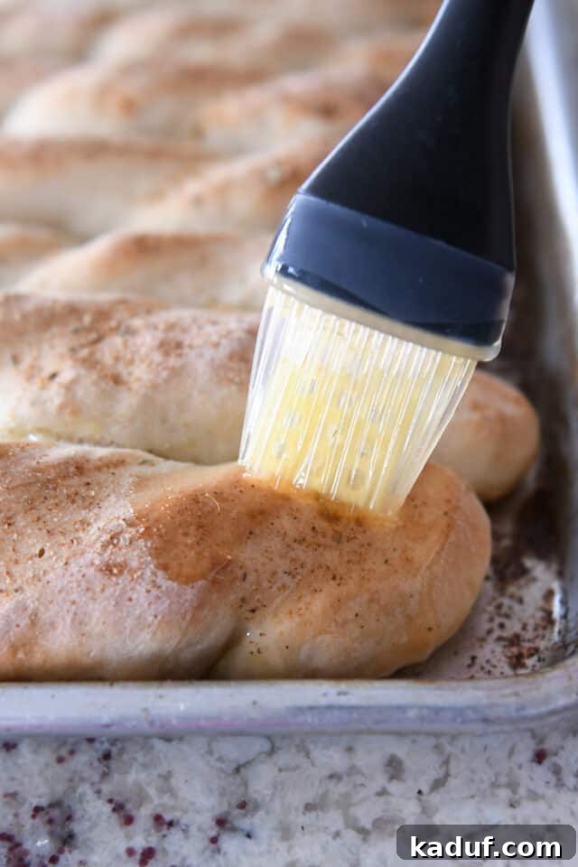 Heavenly 60-Minute Homemade Breadsticks 6 A hand gently brushing melted butter over a freshly baked, warm homemade breadstick, adding a luxurious sheen and enhanced flavor.