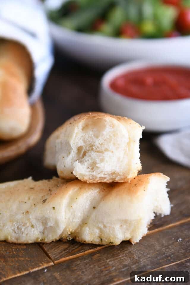 Heavenly 60-Minute Homemade Breadsticks 8 A single, perfectly baked breadstick, torn in half to reveal its soft, airy interior, resting on a rustic wooden board.