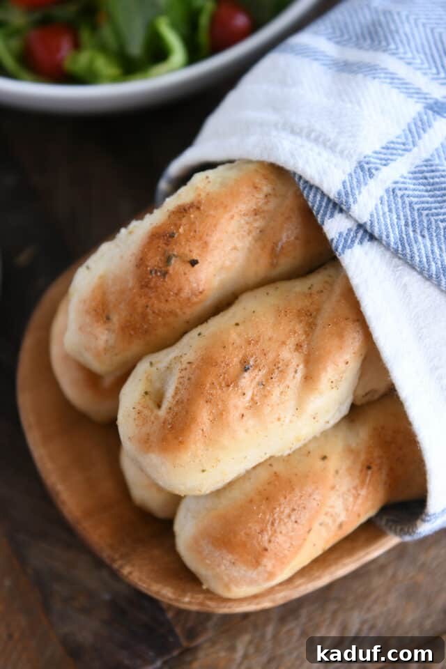 Heavenly 60-Minute Homemade Breadsticks 9 A stack of warm, buttered homemade breadsticks nestled in a cozy kitchen towel on a wooden board, steam gently rising.