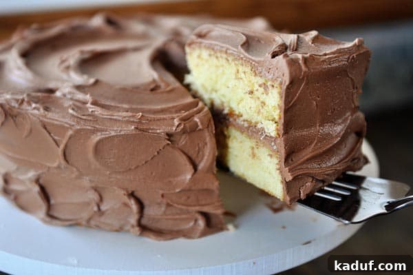 The Gold Standard Homemade Yellow Cake 3 A decadent slice of moist yellow cake with chocolate frosting being lifted from the cake with a fork, showcasing its tender crumb.