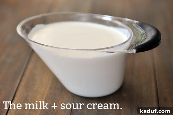 The Gold Standard Homemade Yellow Cake 8 A liquid measuring cup containing a perfectly mixed blend of milk and sour cream, ready to be incorporated into the yellow cake batter for enhanced moisture and tenderness.