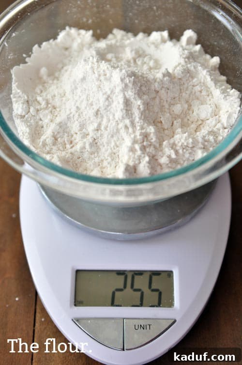 The Gold Standard Homemade Yellow Cake 9 A glass bowl of cake flour, precisely measured on a kitchen scale, highlighting the accuracy required for a finely textured, fluffy yellow cake.
