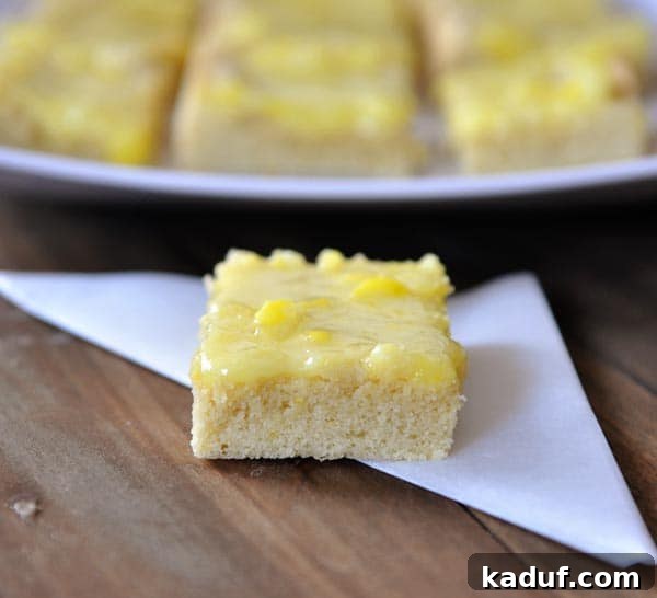 Zesty Lemon Drop Sugar Cookie Bars 2 A tray of Lemon Drop Sugar Cookie Bars, with one bar cut and garnished with vibrant yellow lemon drop candies.