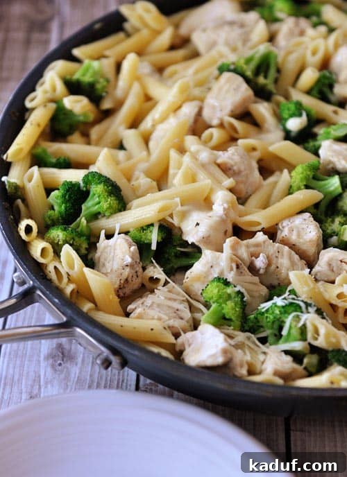Top view of a skillet full of a chicken pasta broccoli meal sprinkled with parmesan cheese.