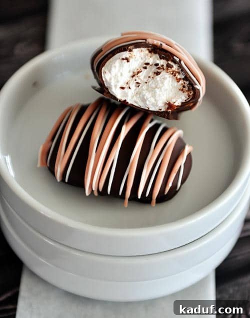 Pillowy Marshmallow Easter Eggs from Scratch 3 Two chocolate covered and chocolate drizzled marshmallow eggs on white plates. The top marshmallow egg has a bite taken out, showing the soft interior.