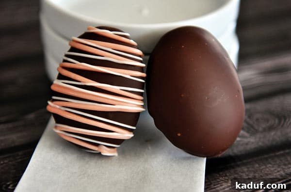 Pillowy Marshmallow Easter Eggs from Scratch 6 Two chocolate covered marshmallow eggs sitting against a stack of white plates, showcasing their elegant appearance.