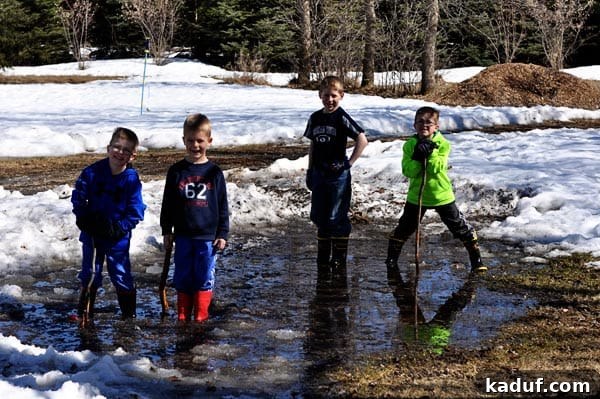 Saturday Stills 4 Four lively young boys playing joyfully in icy, muddy puddles after snowmelt, capturing the essence of outdoor childhood and a mom's perspective on the mess.