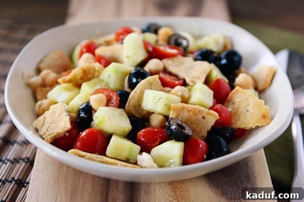 Crispy Greek Pita Salad 2 A white bowl full of pita cubes, olives, cucumbers, and tomatoes with a light dressing. A delicious and healthy Greek Pita Salad.