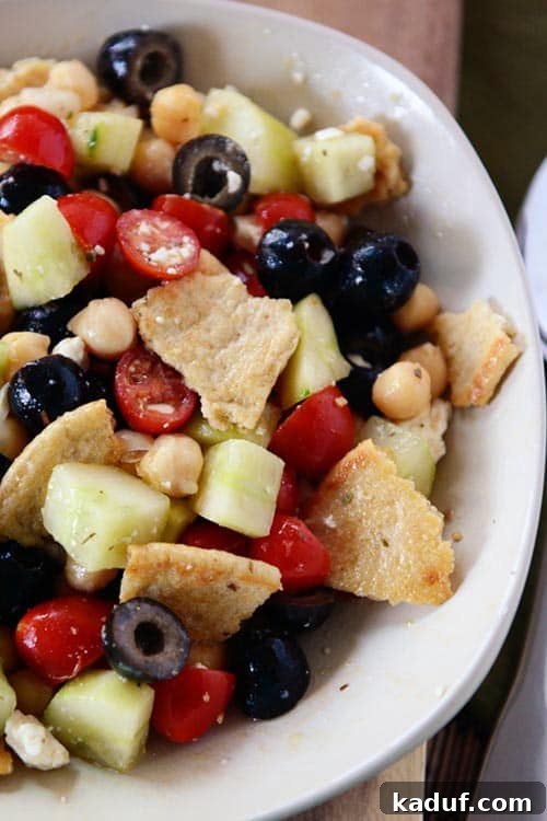Crispy Greek Pita Salad 3 Top view of a white bowl of Greek pita salad filled with toasted pitas, fresh cucumbers, briny olives, juicy tomatoes, and wholesome chickpeas. A light and refreshing meal.
