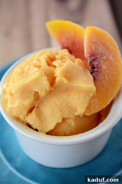 Effortless Healthy Peach Frozen Yogurt 2 A small white ramekin with generous scoops of fresh, creamy peach frozen yogurt, garnished with a few frozen peach slices.