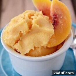 Effortless Healthy Peach Frozen Yogurt 4 Creamy peach frozen yogurt in a small white bowl with peach slices.