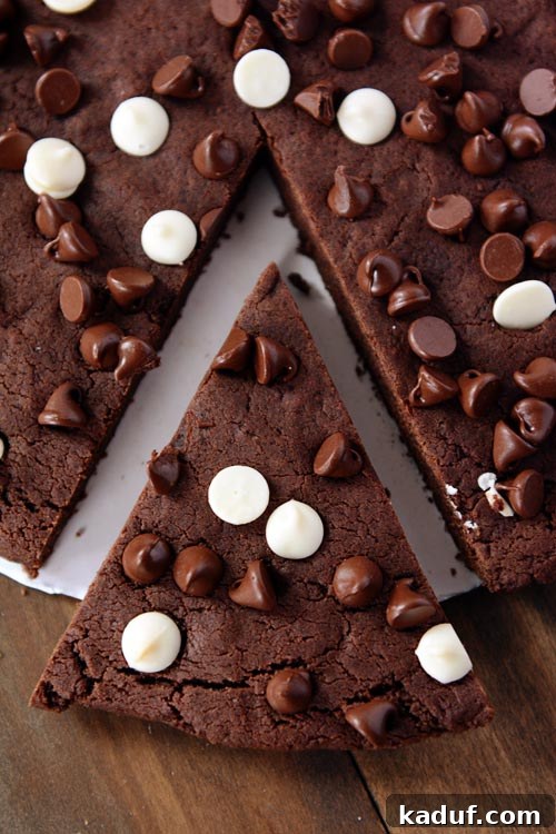 Colossal Double Chocolate Indulgence 4 A pie shaped piece cut out of a giant chocolate chip studded chocolate cookie, ready for serving.