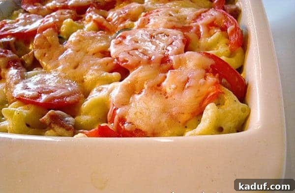 Baked Tuscan Mac and Cheese 2 Close-up of baked macaroni and cheese with sliced tomatoes on top in a white ceramic dish, ready to serve.