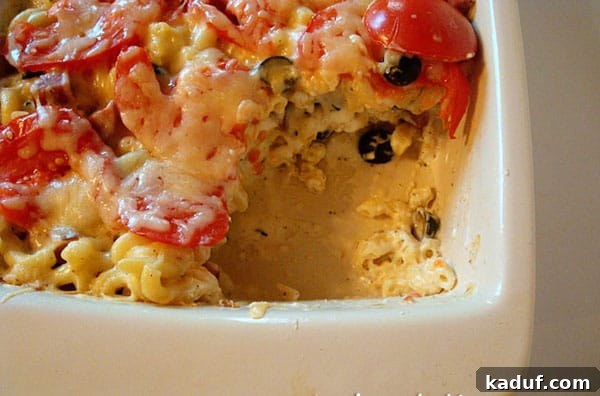Baked Tuscan Mac and Cheese 3 A serving of Tuscan Macaroni and Cheese Bake scooped from a white ceramic dish, showcasing the creamy pasta, chicken, and tomatoes.