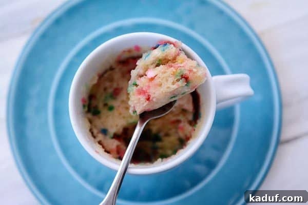 Vegan Vanilla Funfetti Mug Cake 3 Top view of a spoon taking a bite out of a warm, fluffy vanilla funfetti mug cake, showing its moist texture.