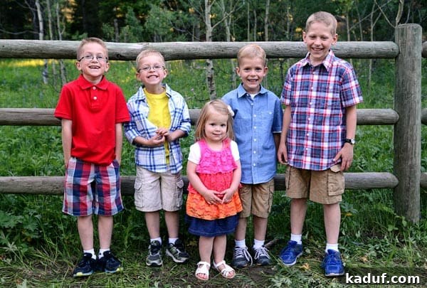 Five little kids burst into laughter against a rustic wooden fence during a family reunion, embodying pure childhood joy.