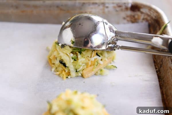 Cheesy Zucchini Gems 5 A cookie scoop putting a mound of cheesy uncooked zucchini batter on a cookie sheet.