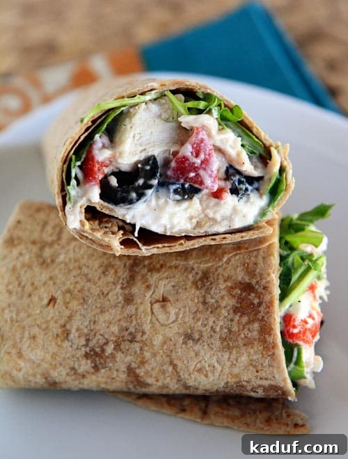 Easy 15-Minute Mediterranean Chicken Wraps 2 A vibrant Mediterranean chicken wrap, sliced in half, showcasing fresh ingredients like chicken, feta, and vegetables on a white plate.