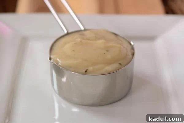 A metal measuring cup full of cream of chicken soup, illustrating its rich texture.