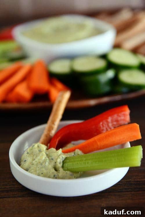 Creamy Zucchini Hummus 3 A beautifully presented tray featuring an assortment of colorful cut vegetables and zucchini hummus, with a small white ramekin holding extra hummus and veggie sticks.