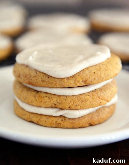 Pillowy Spiced Pumpkin Glaze Cookies 3 A charming stack of frosted pumpkin sugar cookies on a white plate, ready to be served as a delightful autumn dessert or snack.