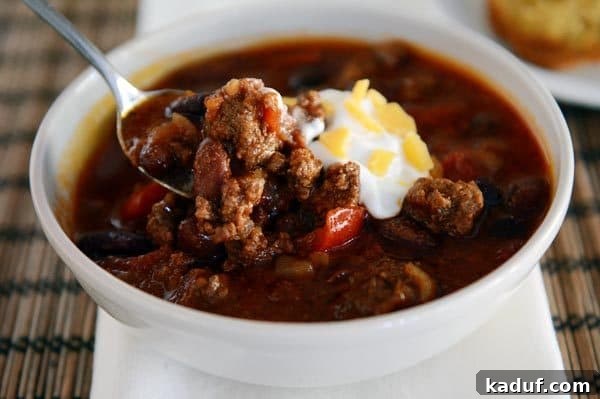 Rich & Hearty Slow-Cooked Chili 9 A beautifully presented white bowl of rich beef chili, perfectly adorned with a swirl of sour cream and a generous sprinkle of shredded cheese.