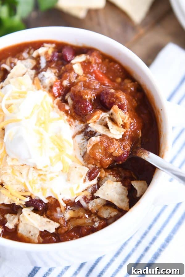 Rich & Hearty Slow-Cooked Chili 3 An inviting top-down view of classic slow cooker chili served in a white bowl, generously topped with shredded cheese and a dollop of sour cream.