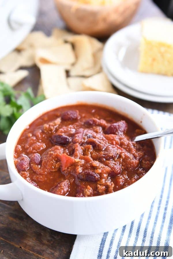 Rich & Hearty Slow-Cooked Chili 6 A close-up of a white bowl filled with classic slow cooker chili, accompanied by a spoon ready for enjoyment.