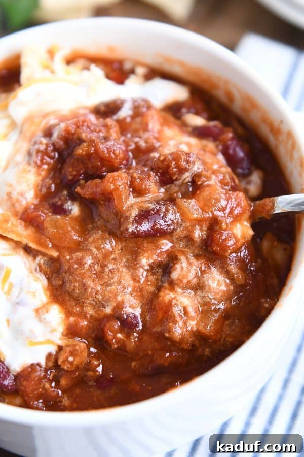 Rich & Hearty Slow-Cooked Chili 7 A hand gently scooping a spoonful of rich classic slow cooker chili from a white bowl, ready to be enjoyed.